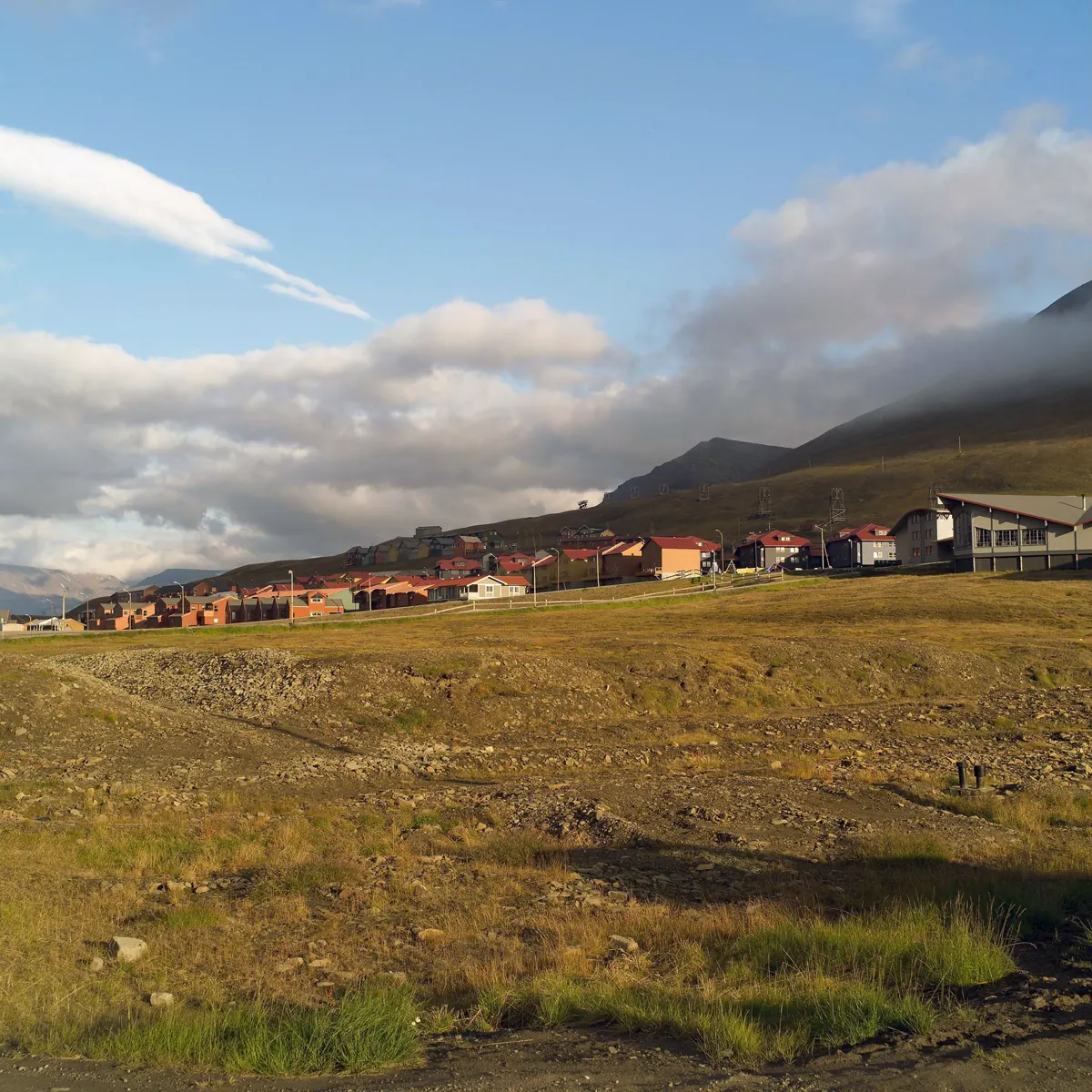 Bunte Wohnhäuser in Longyearbyen, dahinter ein baumloser Hang unter tiefen Wolken.