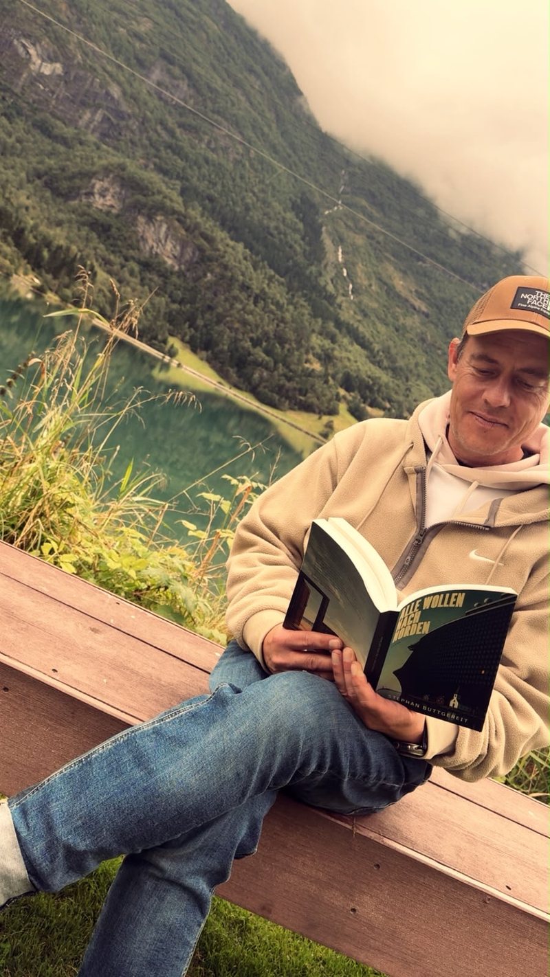Stephan Buttgereit liest Alle wollen nach Norden auf einer Bank am Floen bei Olden, dahinter der See und bewaldete Berghänge